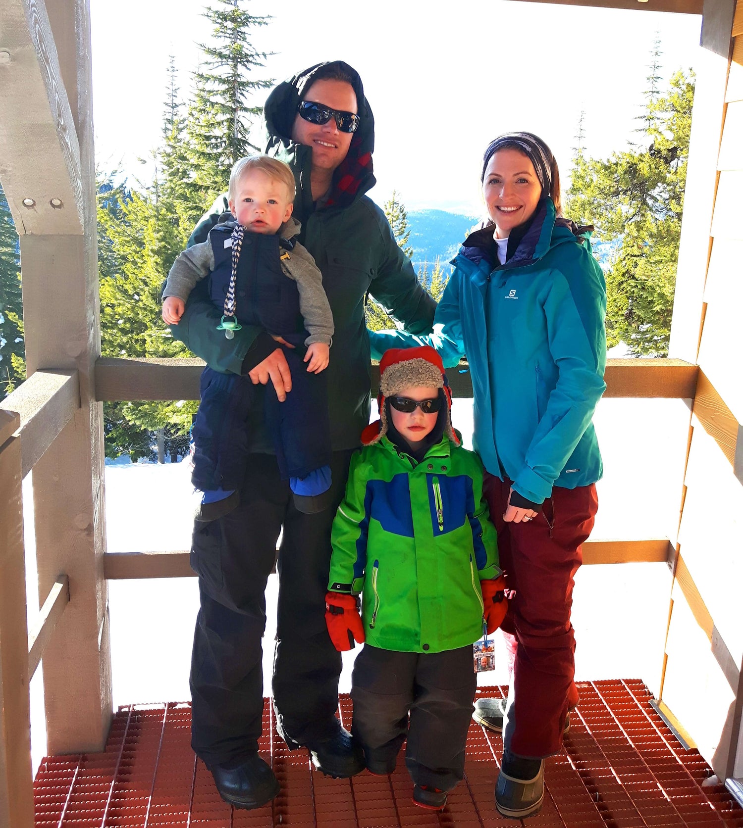 A family of four with young children standing at the top of a mountain on a winter day.