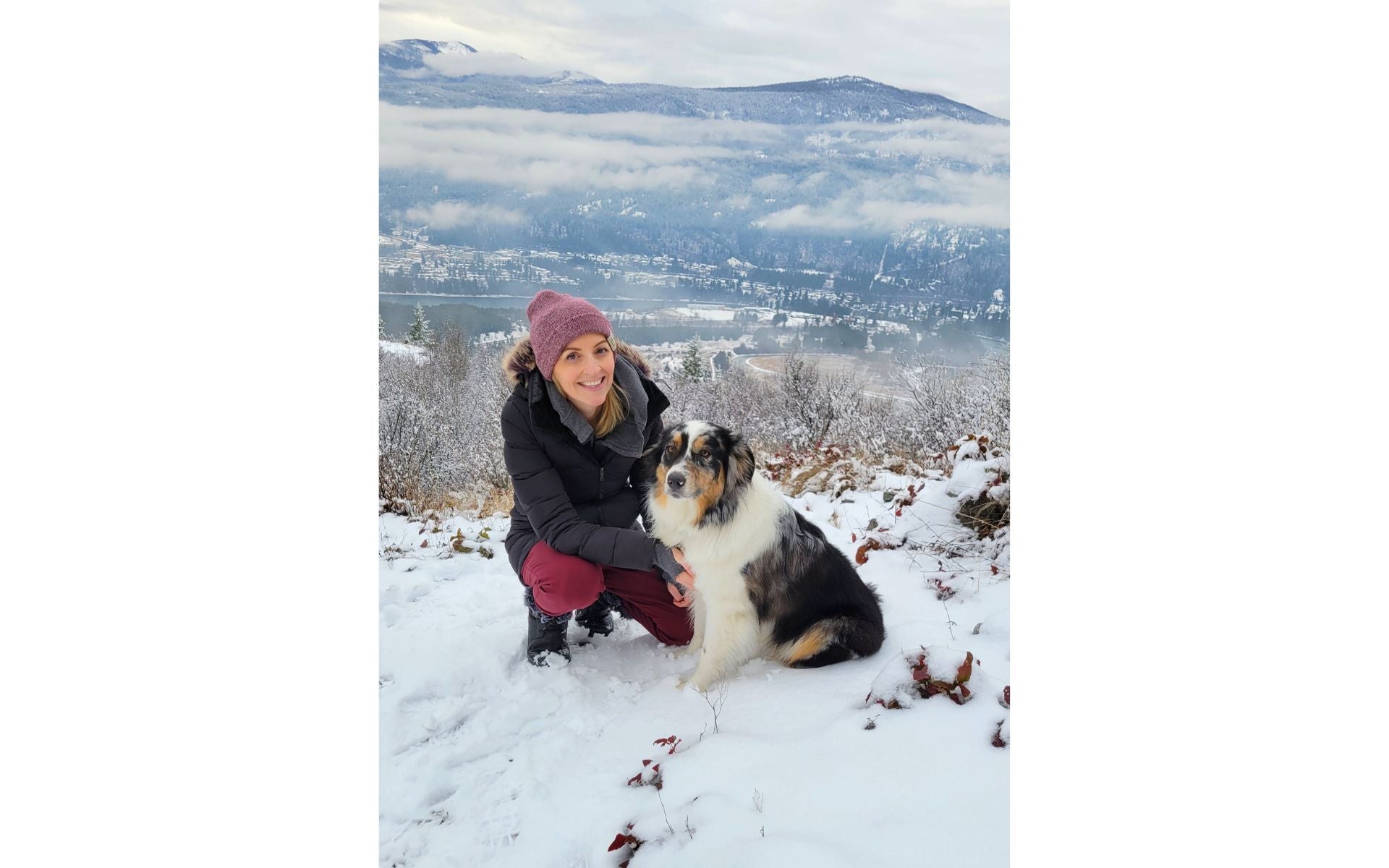 Robyn Phelan standing at the top of a snowy mountain in Castlegar during a winter hike with her dog.